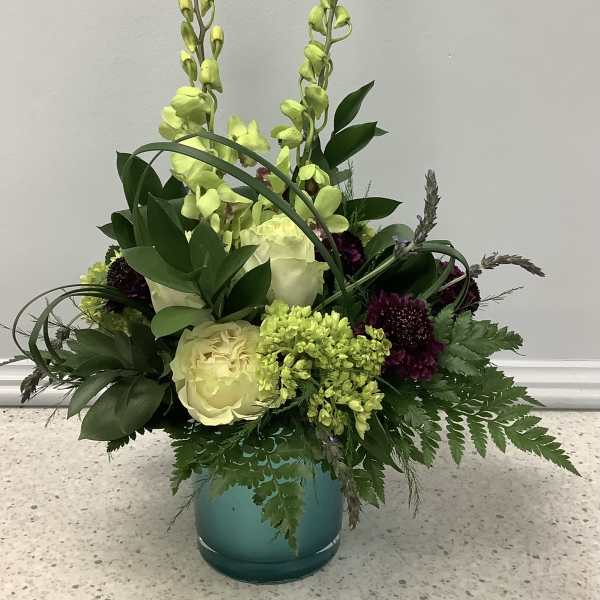 Tall floral arrangement in a teal vase with pale yellow roses and green orchids