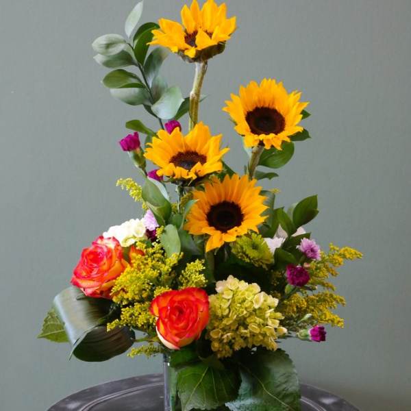 Sunflower and rose arrangement in a square glass vase
