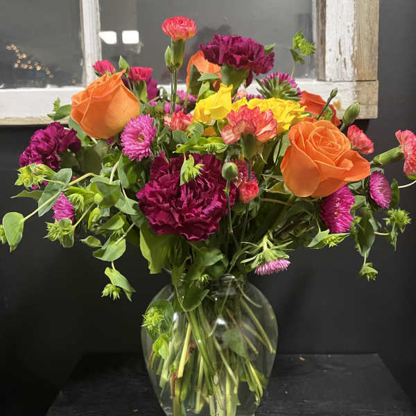 Mixed bouquet of orange roses, magenta carnations, and yellow blooms in a glass vase