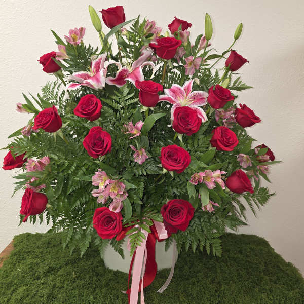 Red roses and pink lilies arranged in a white vase with ribbon