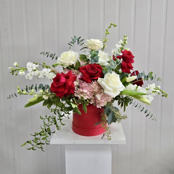 Red and white roses in a red hatbox with trailing greenery