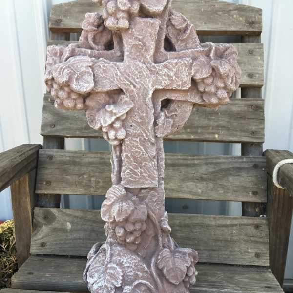 A pink stone cross with floral carvings sits on a wooden chair.