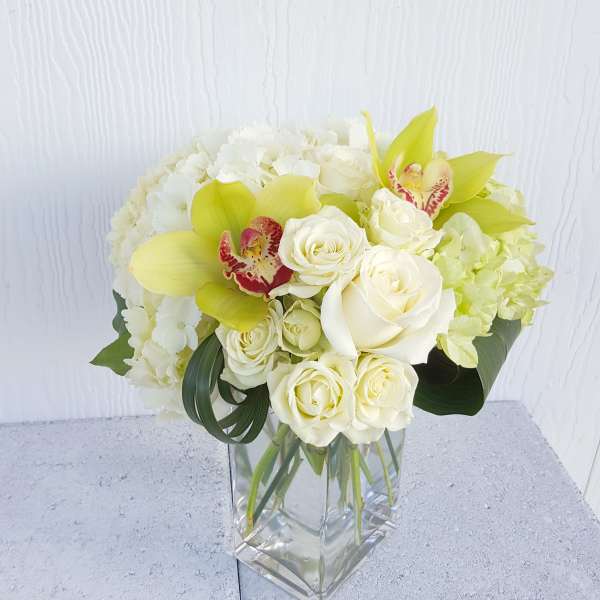White and pale yellow floral arrangement in a clear glass vase
