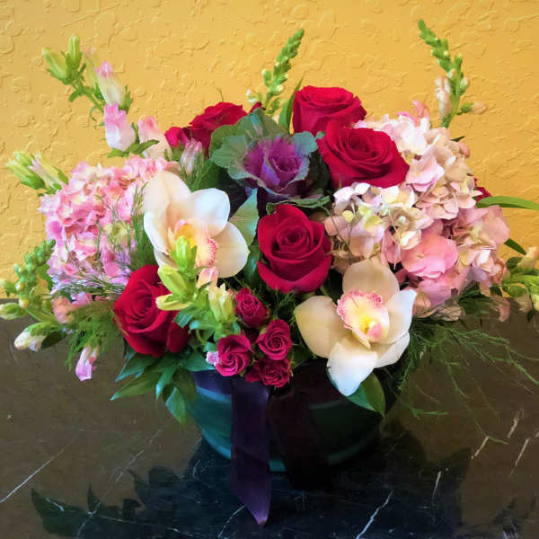 Mixed bouquet of red roses, pink hydrangeas, and white orchids in a black vase