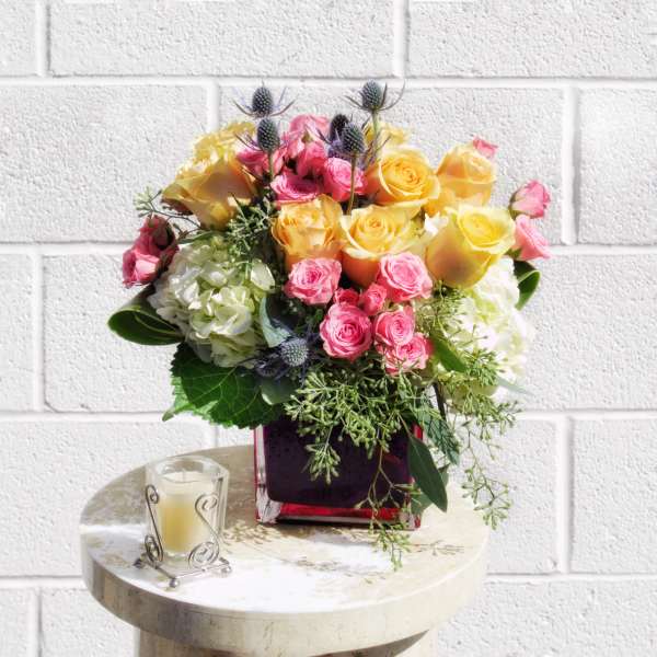 Bouquet of yellow and pink roses in a square vase with a candle beside it