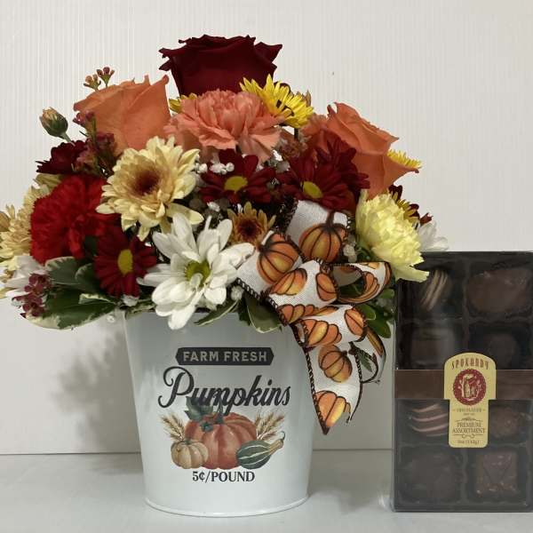 Fall flower arrangement in a pumpkin bucket beside a box of chocolates