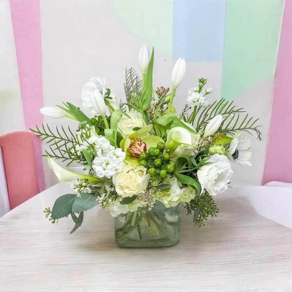 White and green floral arrangement in a square glass vase