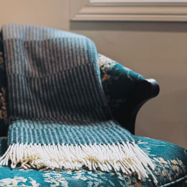 A striped woven blanket draped over a teal floral armchair