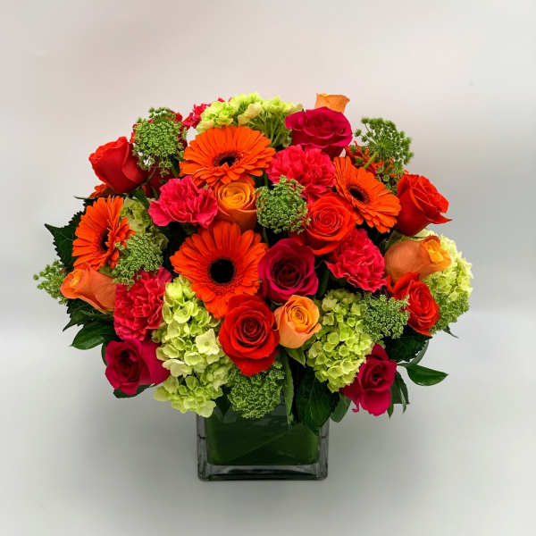 Bright mixed bouquet of roses, gerberas, carnations, and hydrangeas in a glass vase
