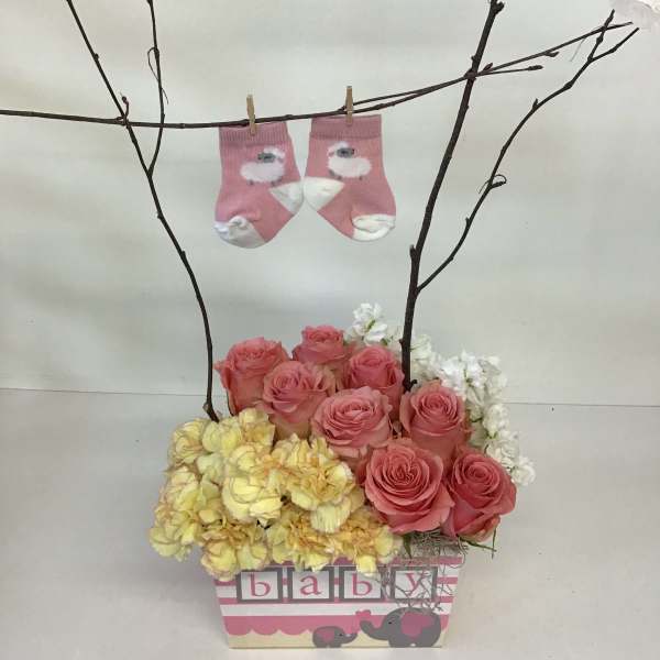 Pink roses and yellow flowers in a baby-themed box with tiny socks on branches
