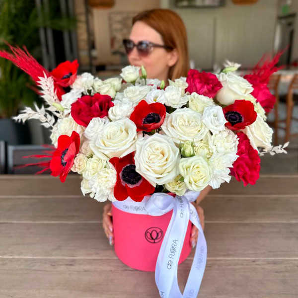 Bouquet of red and white roses with red anemones in a pink hatbox