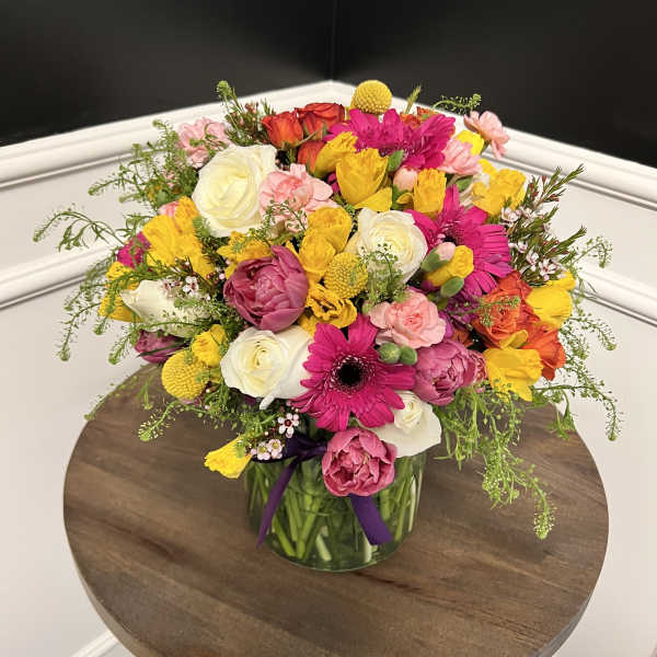 Mixed bouquet of pink, yellow, white, and orange flowers in a glass vase