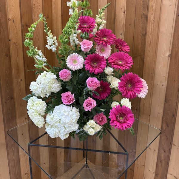 Tall arrangement of hot pink gerberas, pink roses, white hydrangeas, and green bells of Ireland.