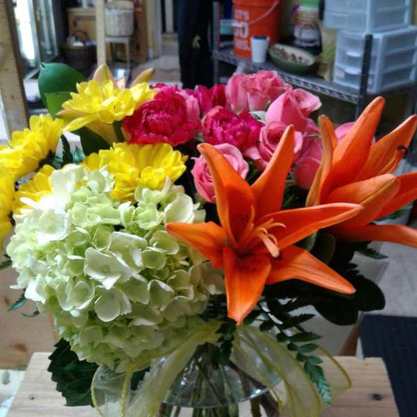 Bouquet of orange lilies, pink roses, yellow daisies, and pale hydrangea in a glass vase