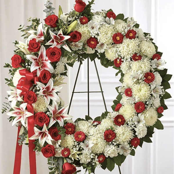 Heart-shaped floral wreath with red roses and white flowers on a stand