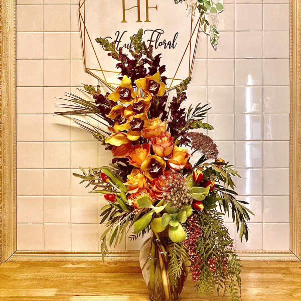 Tall floral arrangement in a glass vase with orange and burgundy blooms