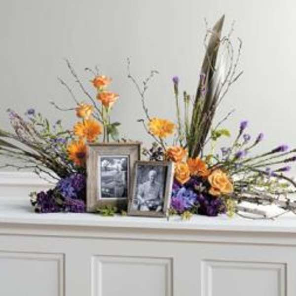 Floral memorial arrangement with framed photos on a white surface