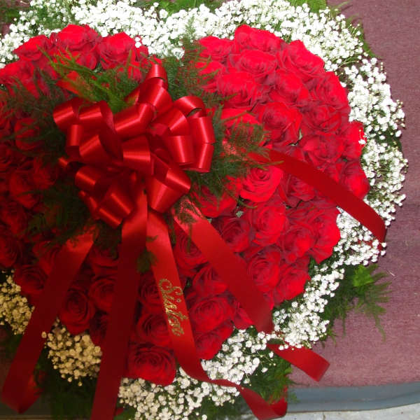 Heart-shaped arrangement of red roses with white baby's breath and a red ribbon bow