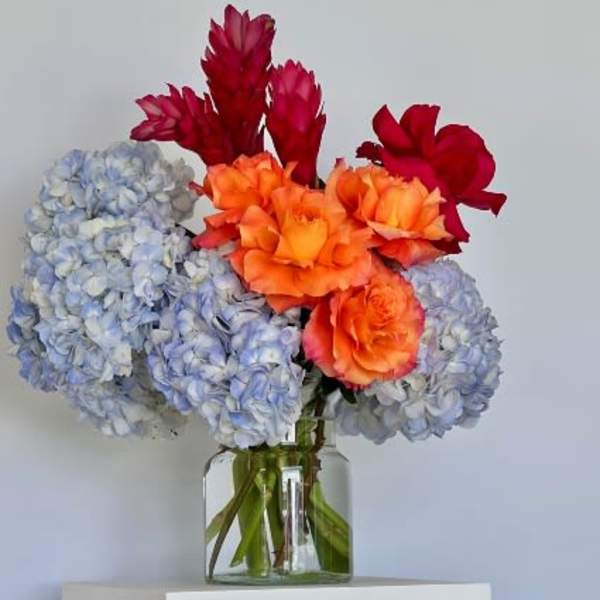 Bouquet of blue hydrangeas and orange-red flowers in a glass vase