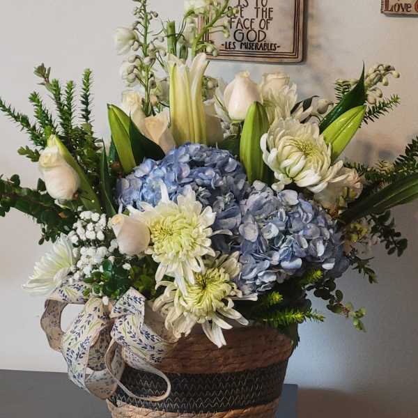 Basket arrangement with blue hydrangeas, white lilies, and pale roses