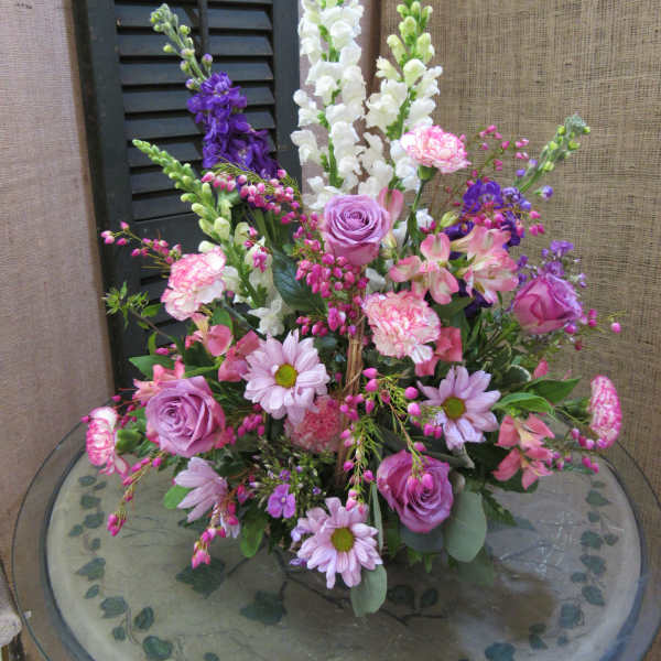 Mixed pink and purple floral arrangement with tall white spikes in a glass vase