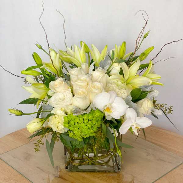 White and pale yellow floral arrangement in a square glass vase
