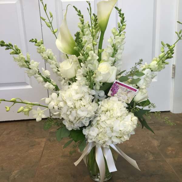 White floral arrangement with calla lilies, roses, and hydrangeas in a glass vase
