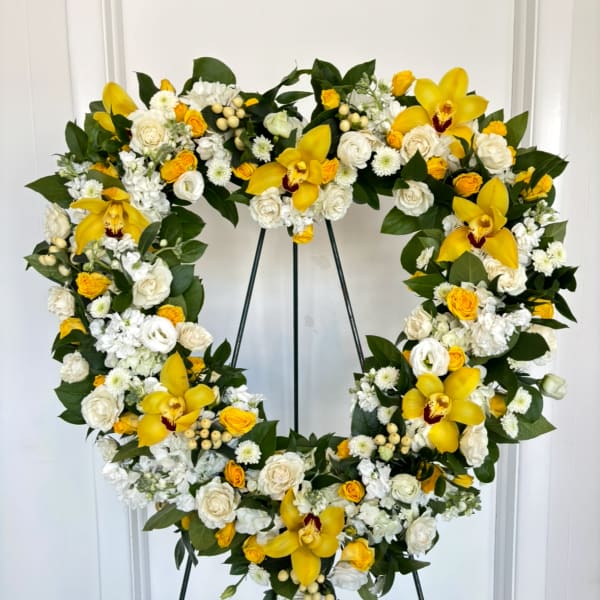 Heart-shaped floral wreath with yellow orchids and white roses on a stand