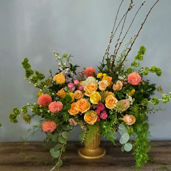 Large mixed flower arrangement in a gold vase with peach and pink blooms
