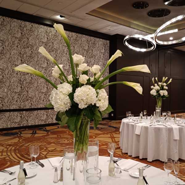 Tall white floral centerpiece in a clear glass vase on a banquet table