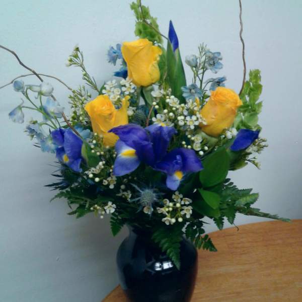 Yellow roses and blue irises in a black vase