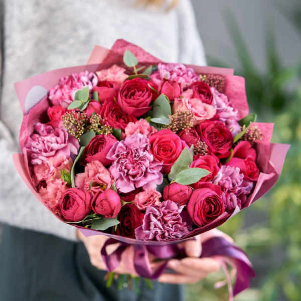 Handheld bouquet of pink and red roses with carnations wrapped in pink paper