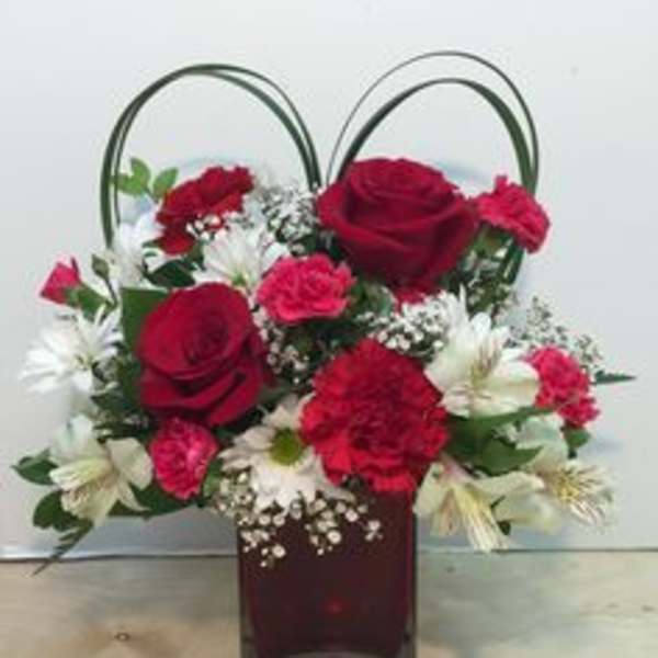 Red roses and carnations in a square glass vase with looped handles