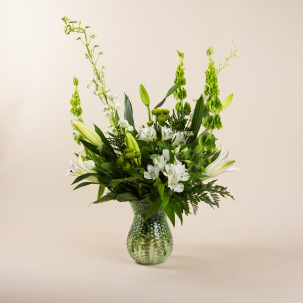 White lilies and green flowers in a textured glass vase