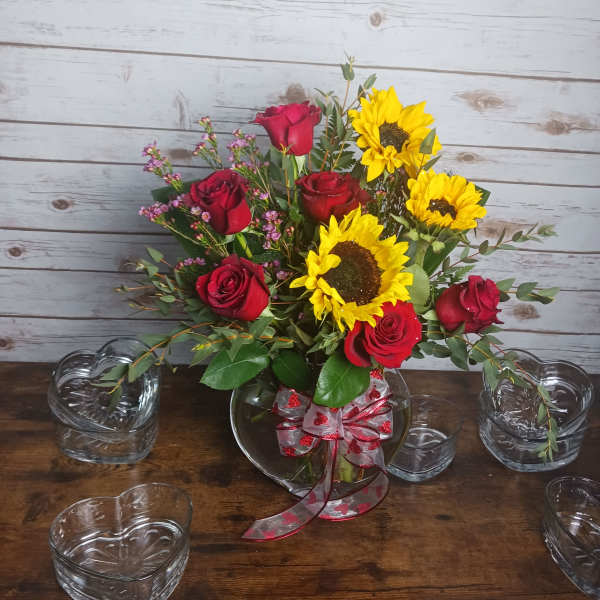 Bouquet of red roses and yellow sunflowers in a glass vase with ribbon