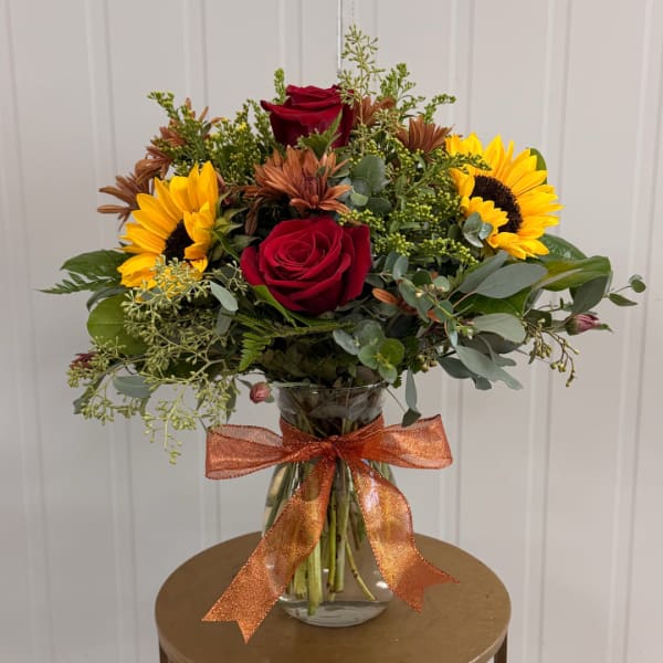 Bouquet of red roses and sunflowers in a glass vase with an orange ribbon