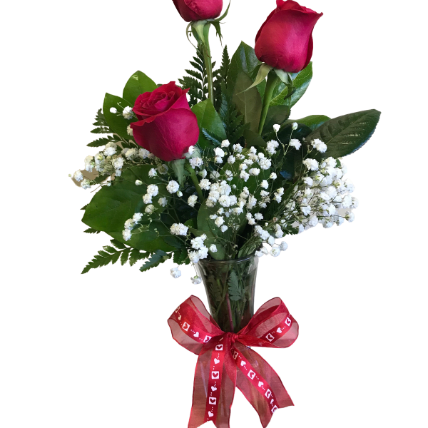 Three red roses in a clear vase with baby's breath and a red ribbon