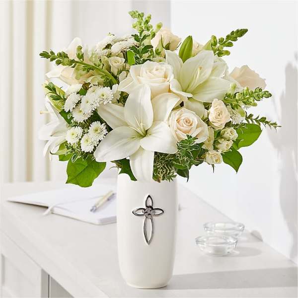 White lilies and cream roses in a white vase with a cross