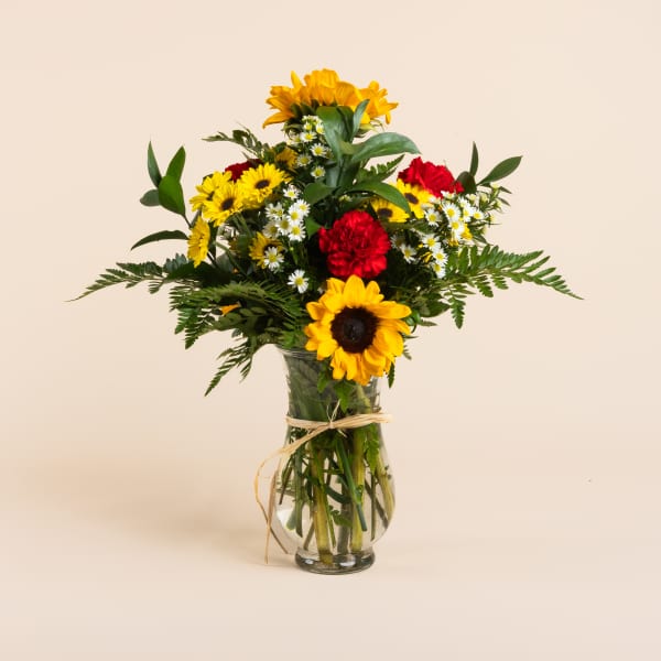 Bouquet of sunflowers, daisies, and red carnations in a glass vase