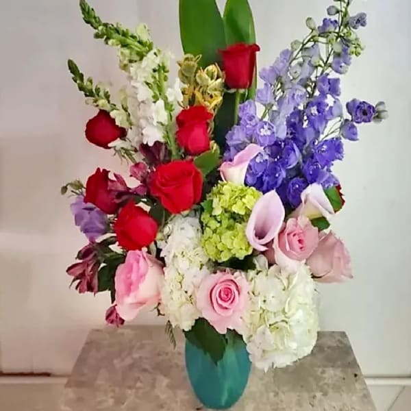 Mixed bouquet of roses, calla lilies, hydrangeas, and delphinium in a teal vase