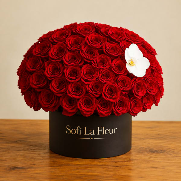 Round arrangement of red roses in a black box with a white orchid accent