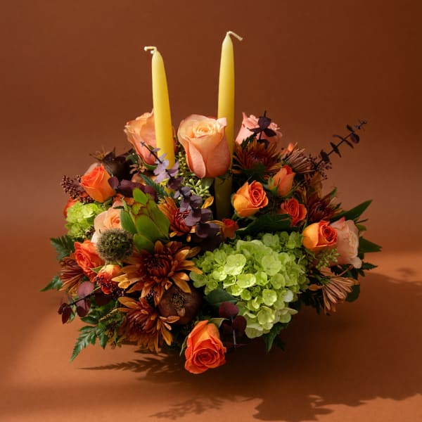 Orange roses and green hydrangeas arranged with two yellow candles
