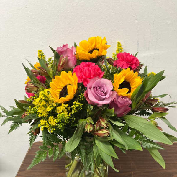 Mixed bouquet of sunflowers, roses, and carnations in a glass vase