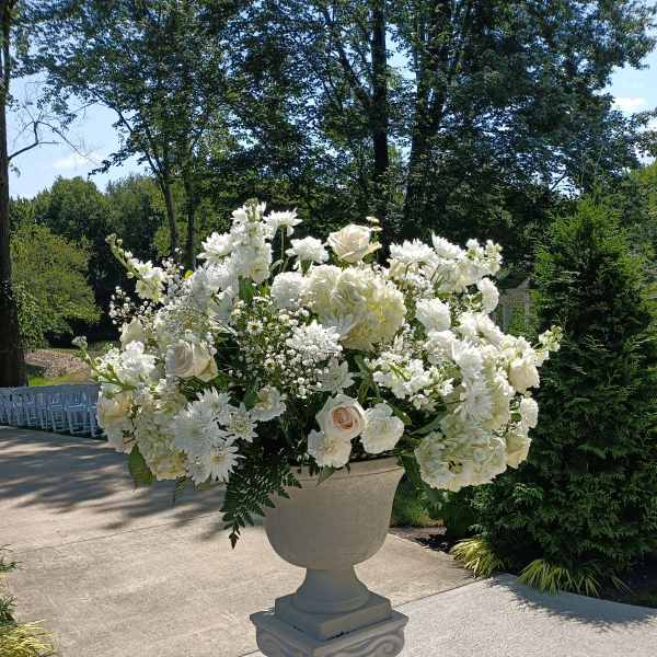 Large white floral arrangement in a pedestal urn outdoors