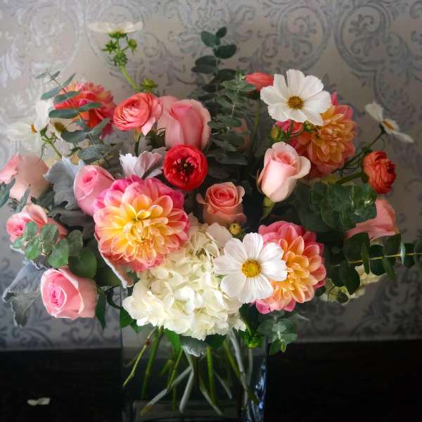 Mixed bouquet of pink roses, white hydrangea, and white daisies in a glass vase