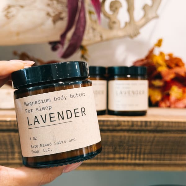 Hand holding a lavender body butter jar with two similar jars behind it