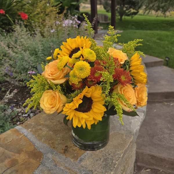 Bouquet of sunflowers, yellow roses, and mums in a glass vase