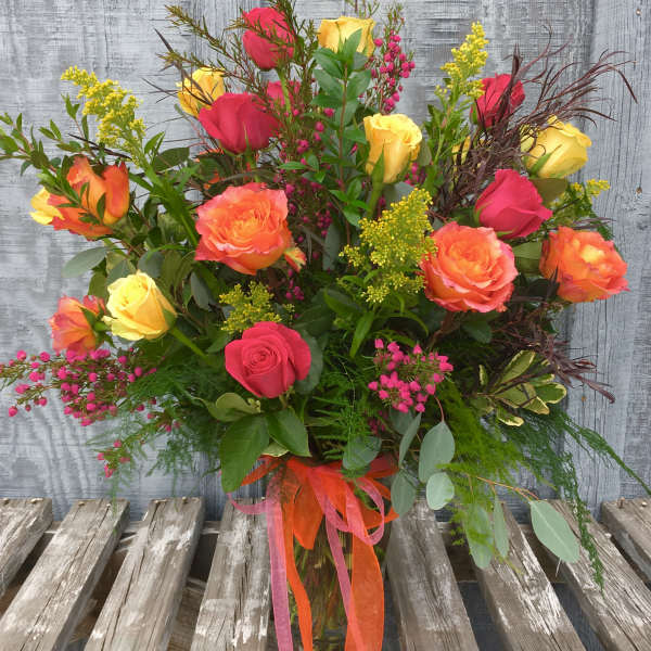 Mixed bouquet of red, yellow, and orange roses in a glass vase
