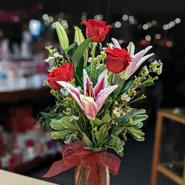 Red roses and pink lilies in a clear glass vase with a red ribbon