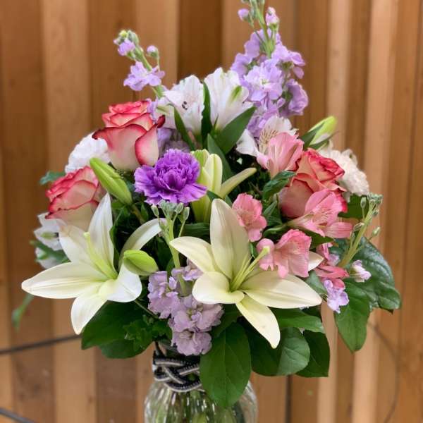Bouquet of lilies, roses, and purple flowers in a glass vase